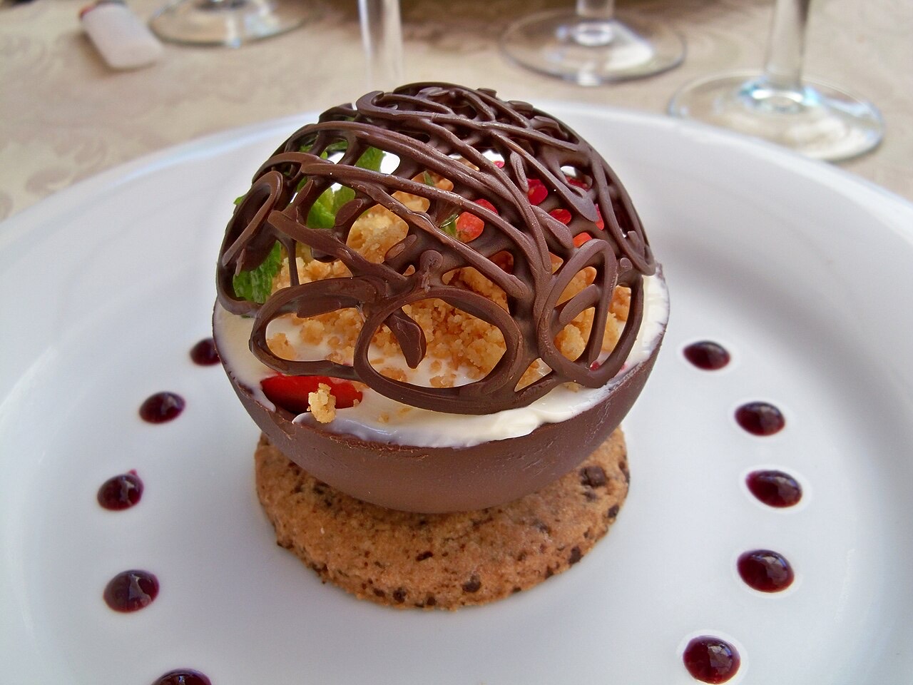 A plated fine-dining chocolate sphere dessert with sauce dots