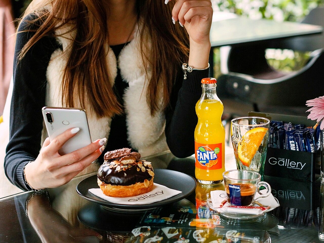 A diner holding a smartphone over a cafe table with dessert and drinks